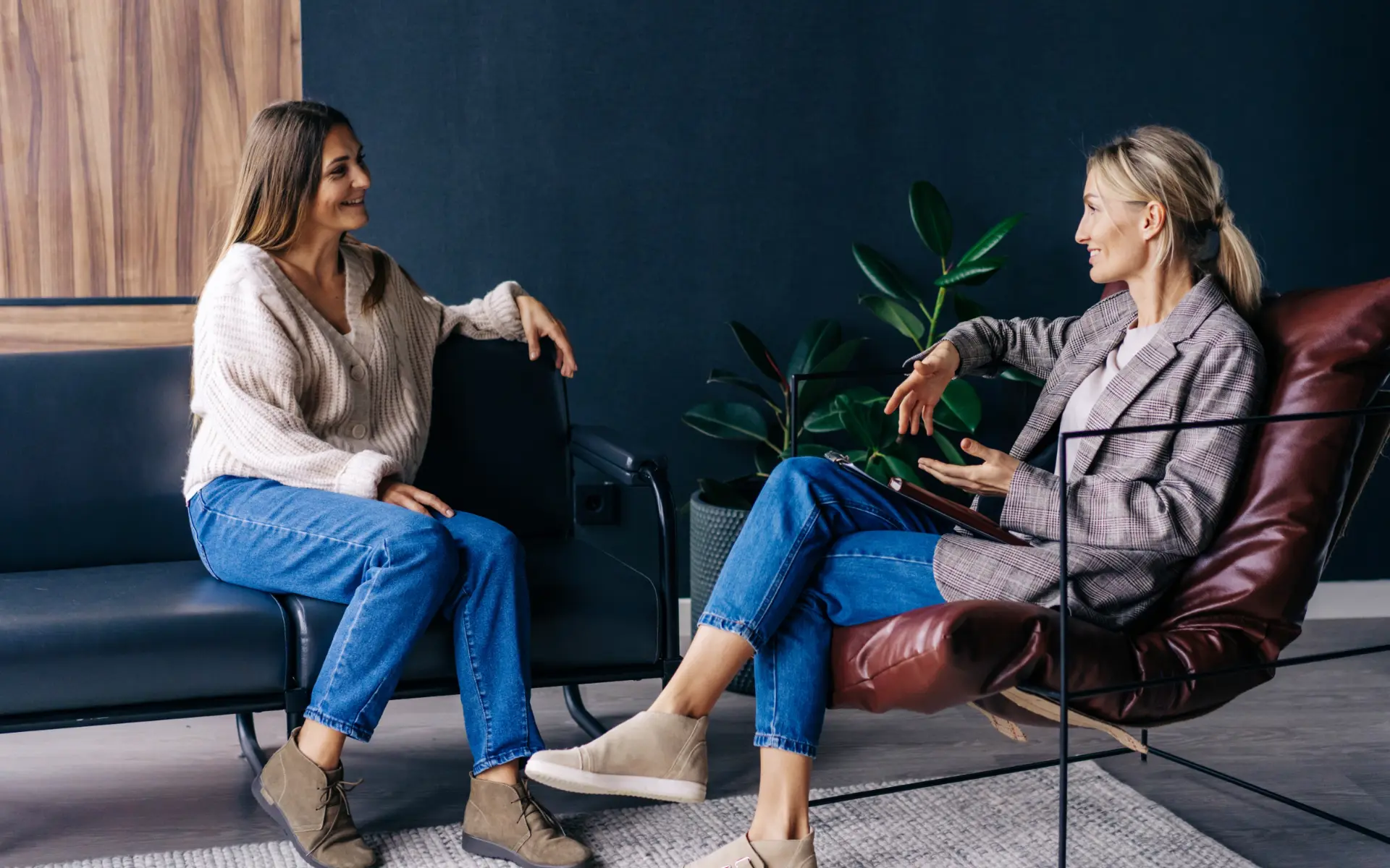 Two women talking in armchairs in a sitting room, one holding a notebook